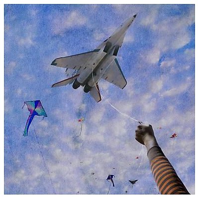 An image designed like an old photo aimed skyward, where a child's outstretched arm holds a fighter jet attached to a string among a smattering of kites.