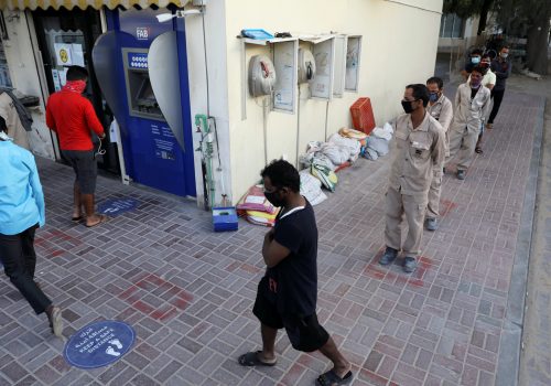 Foreign workers wearing protective face masks queue to use an ATM