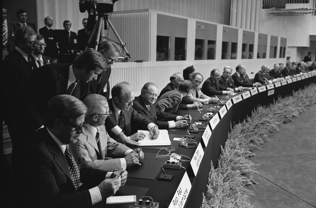 Photograph of President Gerald R. Ford Signing the Final Act of the Conference on Security and Cooperation in Europe as It is Passed Among European Leaders for Signature in  Finlandia Hall in Helsinki, Finland