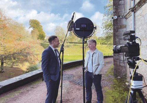 Two men speaking in front of a news camera