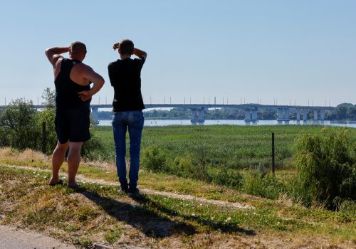 Two men look at the Antonovsky bridge in Kherson, Ukraine, July 27, 2022. It has been damaged by Ukrainian attacks but not destroyed. (Source: REUTERS/Alexander Ermochenko)