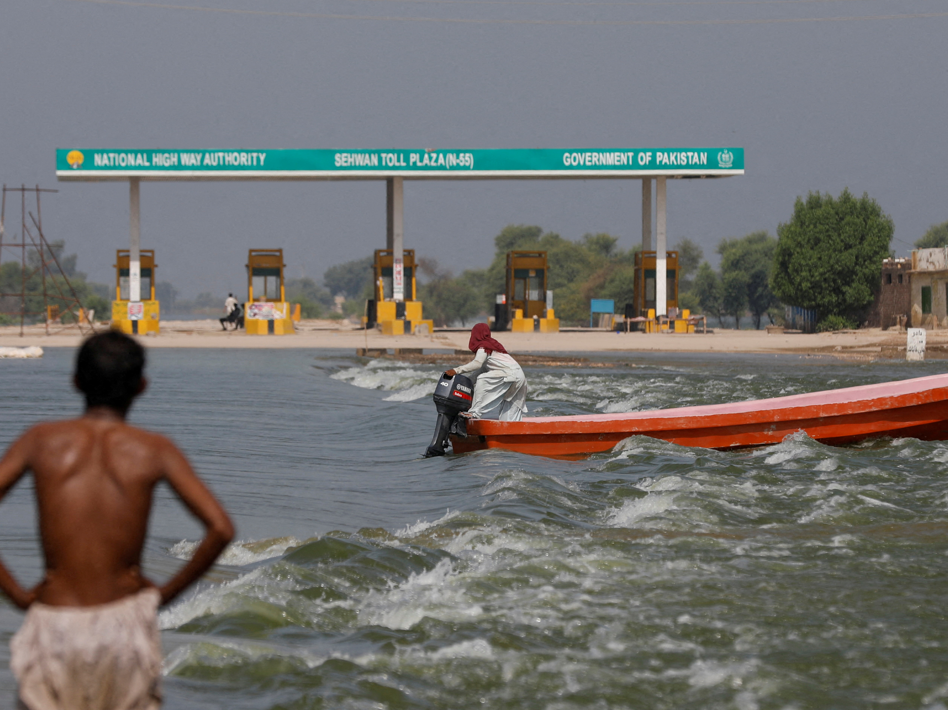 A man rides a boat past toll plaza amid flood water on main Indus highway, following rains and floods during the monsoon season in Sehwan, Pakistan.