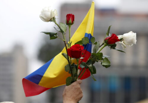 A raised hand holds a Colombian flag and several roses.