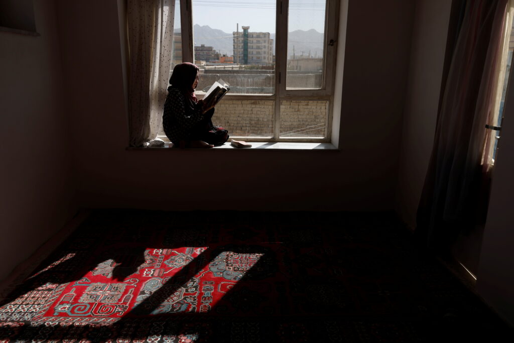 Student reads a book as she sits on a windowsill at her home in Kabul, Afghanistan.