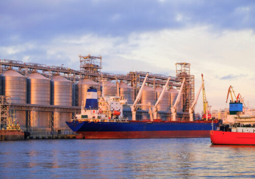 Bulk carrier ship in river port. Dry cargo grain elevator trade. Agrarian maritime facility. Cargo ship in the sea. Sunset view. factory on the water.