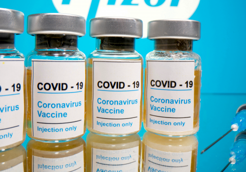 Vials with a sticker reading, “COVID-19 / Coronavirus vaccine / Injection only” and a medical syringe are seen in front of a displayed Pfizer logo in this illustration taken October 31, 2020.